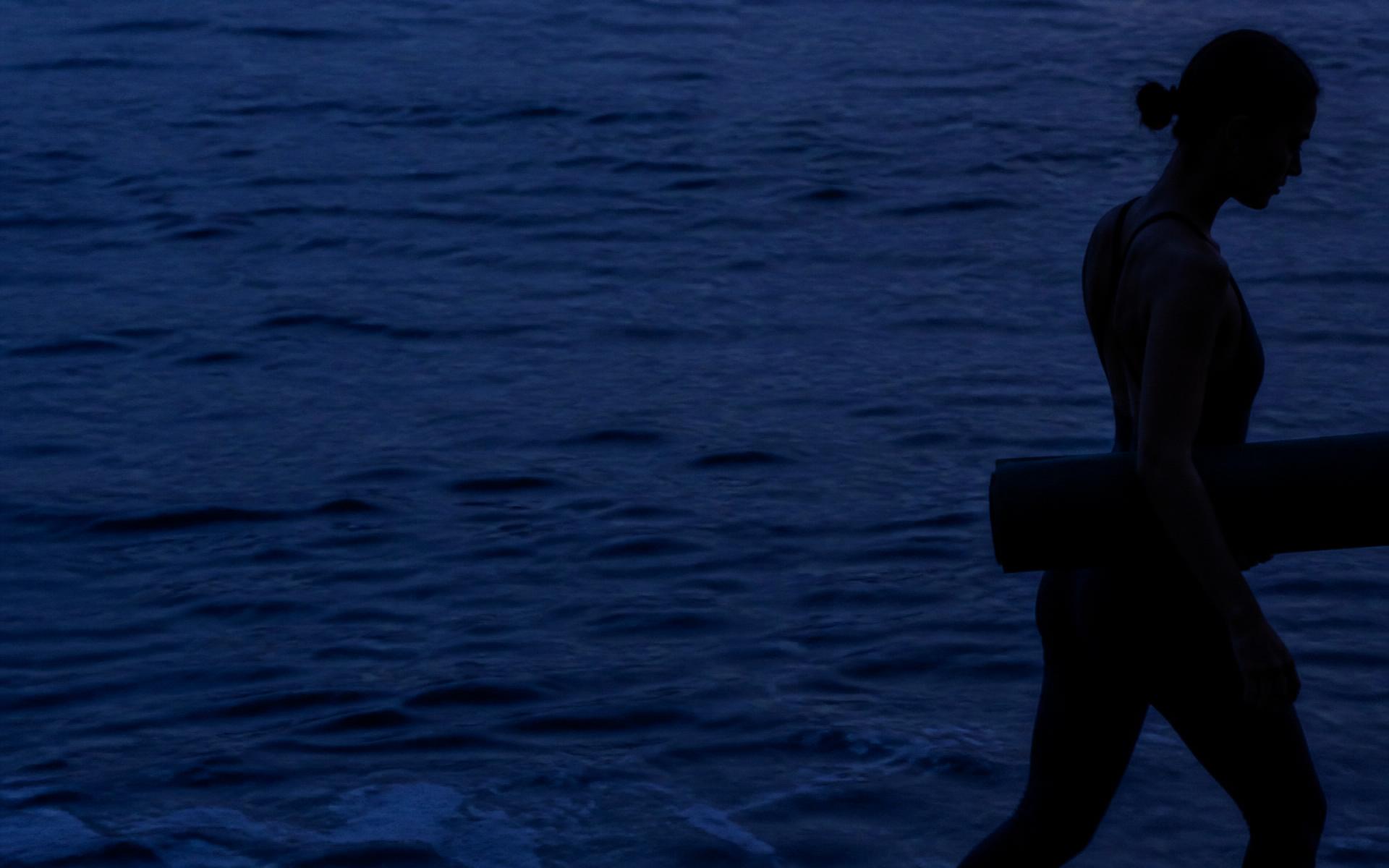 Silhouet van een vrouw met een mat langs het water bij schemer